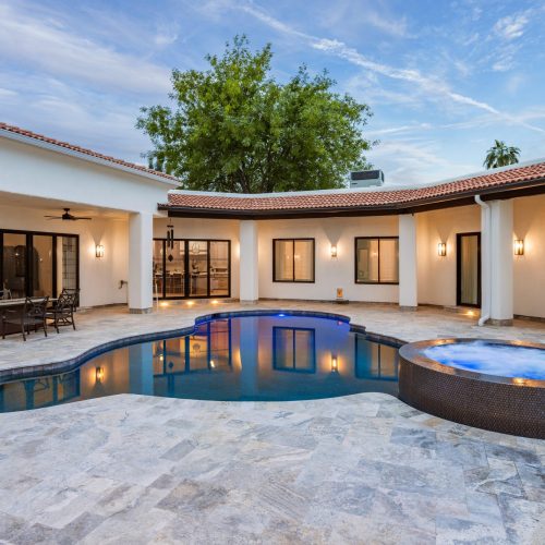 Freeform pool and raised round spa lit at dusk