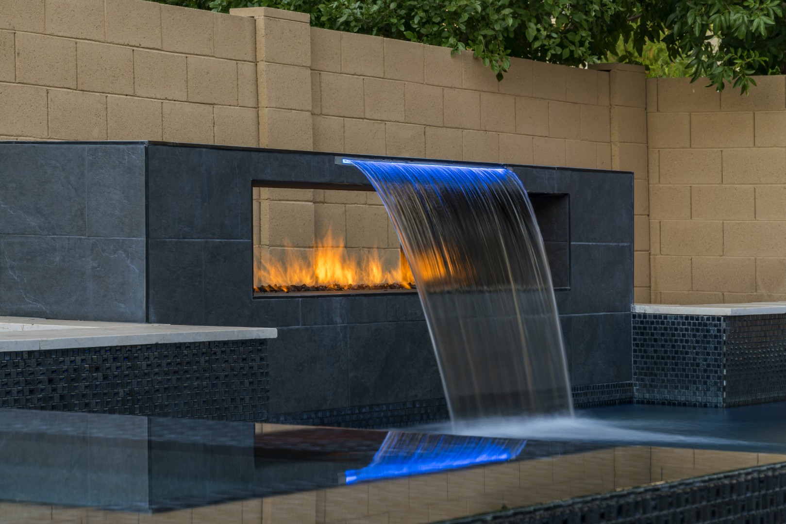 Custom pool with fire and water feature wall, raised spa, and outdoor kitchen in Gilbert, AZ by Envy Pools
