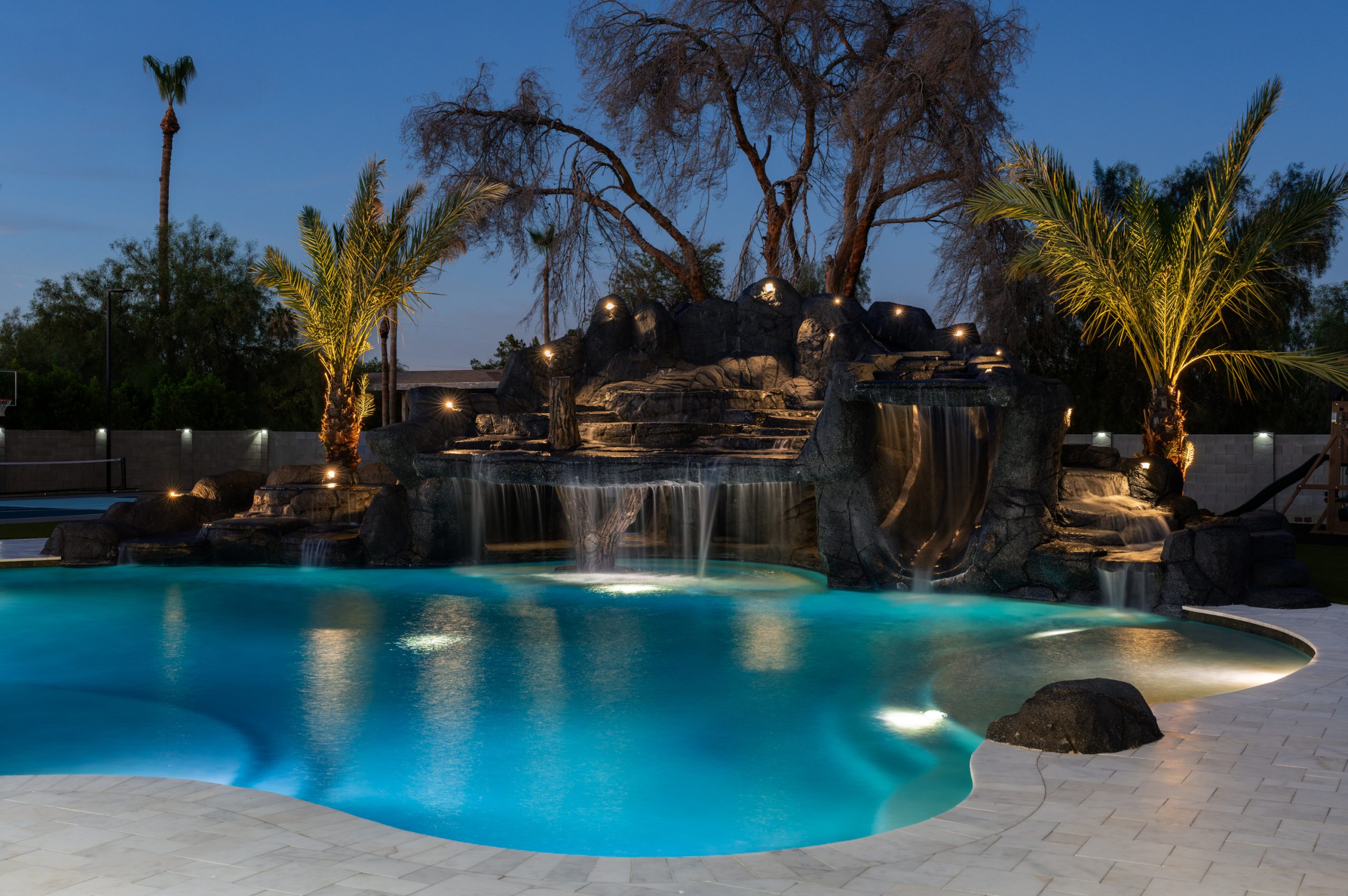 Rock waterfall lit at night over a custom pool in Gilbert, AZ