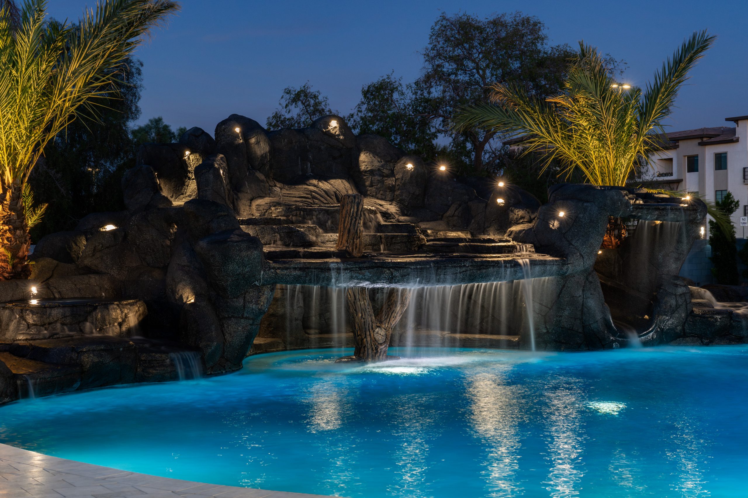 Lit rock waterfall and freeform pool at night in Gilbert, AZ